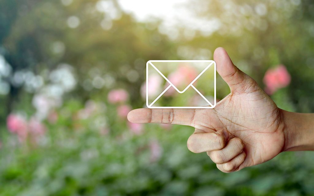 Mail icon on finger over blur pink flower and tree, Contact us concept Mail icon on finger over blur pink flower and tree, Contact us concept